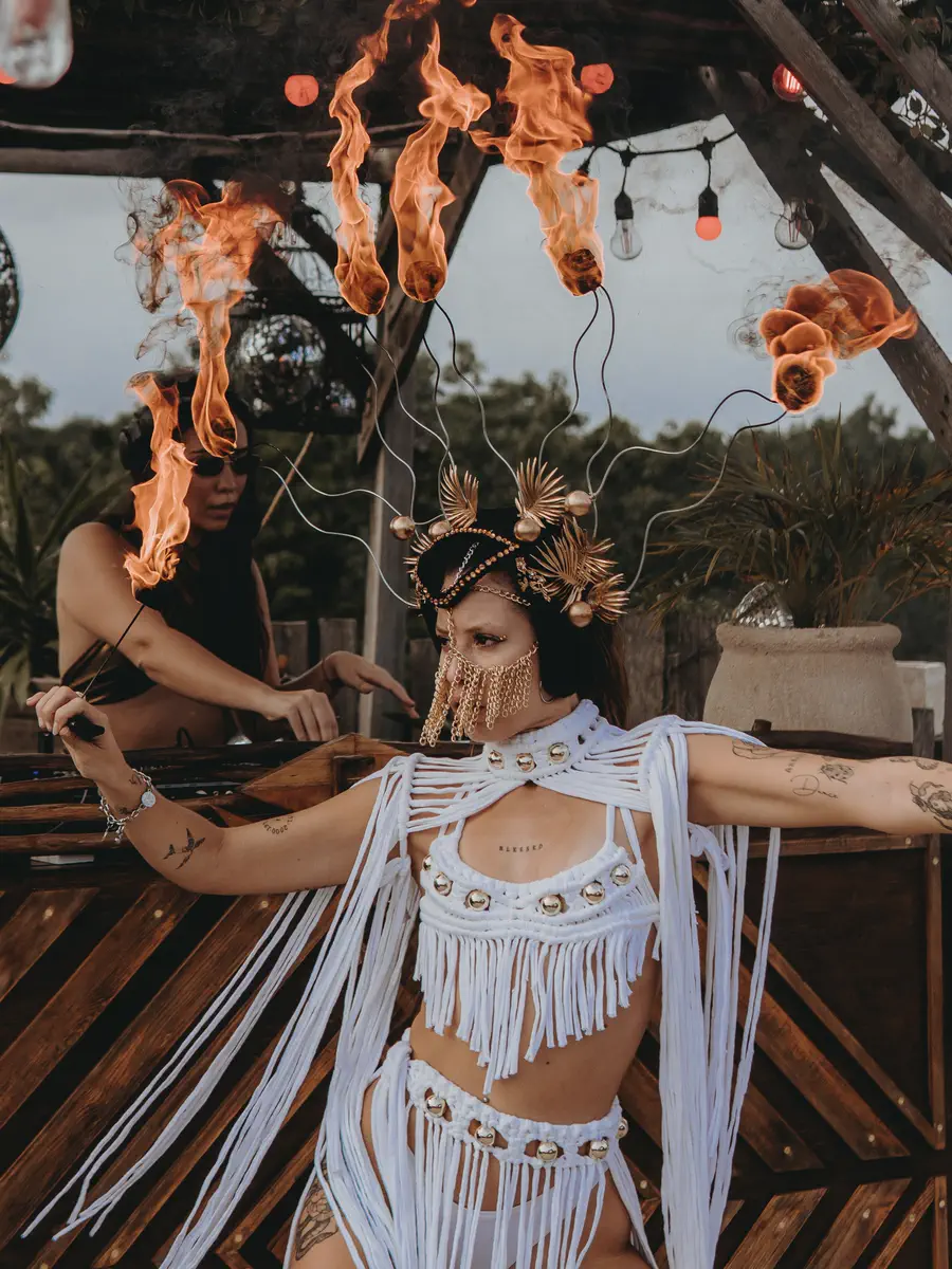 Dos performers con vestuario de flecos blancos y tocados encendidos en un venue al aire libre