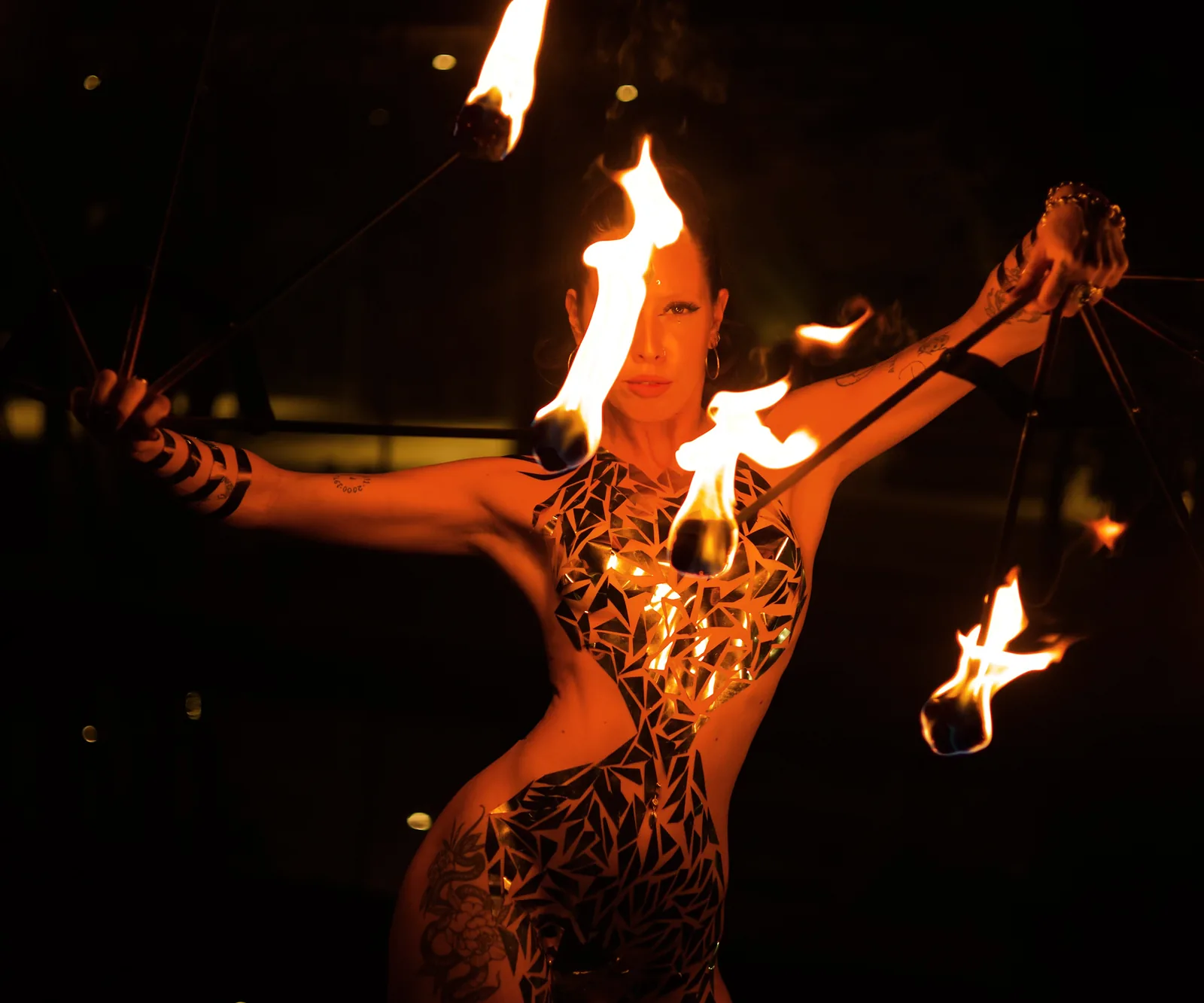 Karu, fundadora de Escena Global, con el cuerpo pintado y abriendo dos abanicos de fuego encendidos de noche