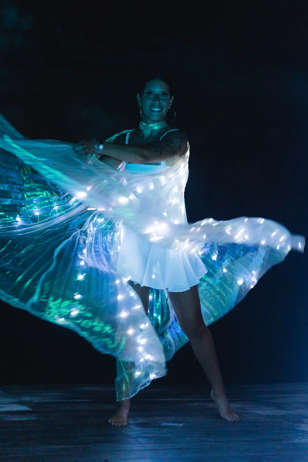 Bailarina con alas de luces LED girando sobre un escenario oscuro